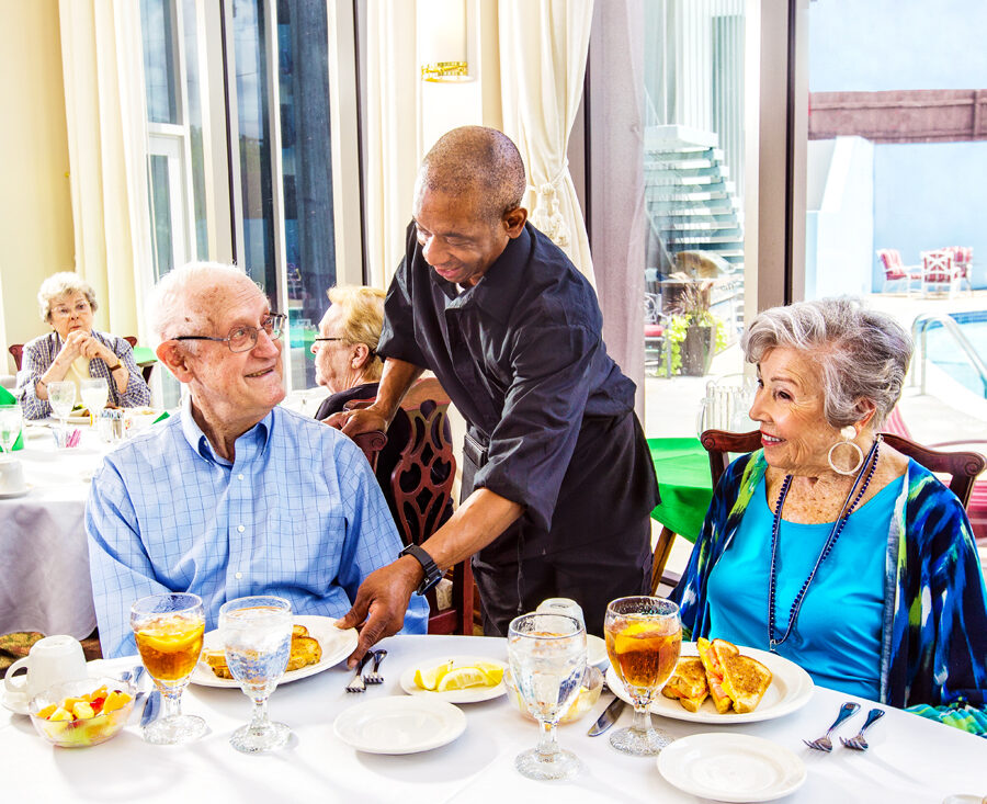 A senior man and woman are served dinner by a young waiter