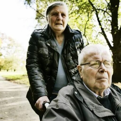 A senior woman pushing her husband in a wheel chair, one of the demands of caregiving