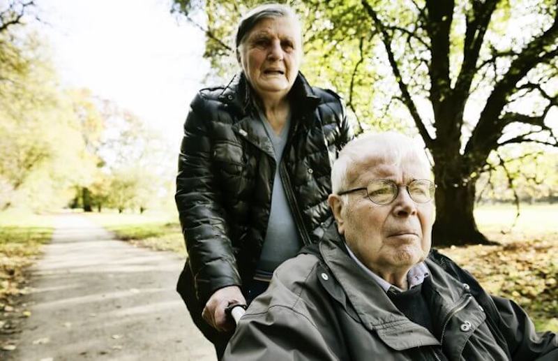 A senior woman pushing her husband in a wheel chair, one of the demands of caregiving