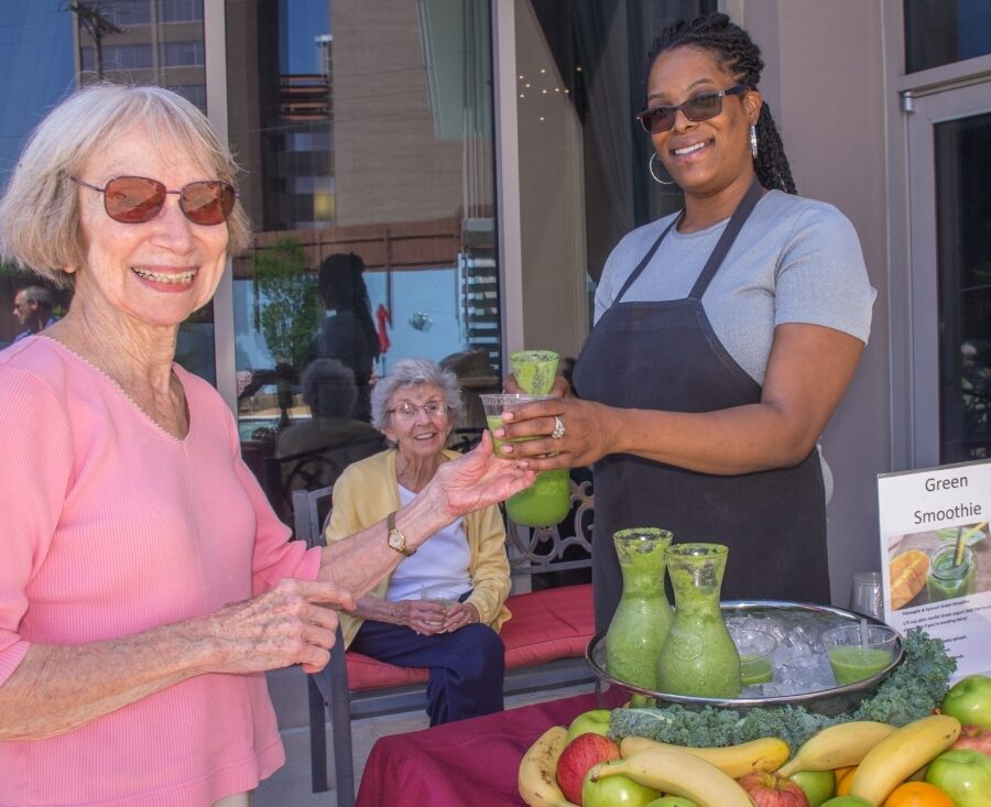 A senior woman receives a smoothie from a young woman outside