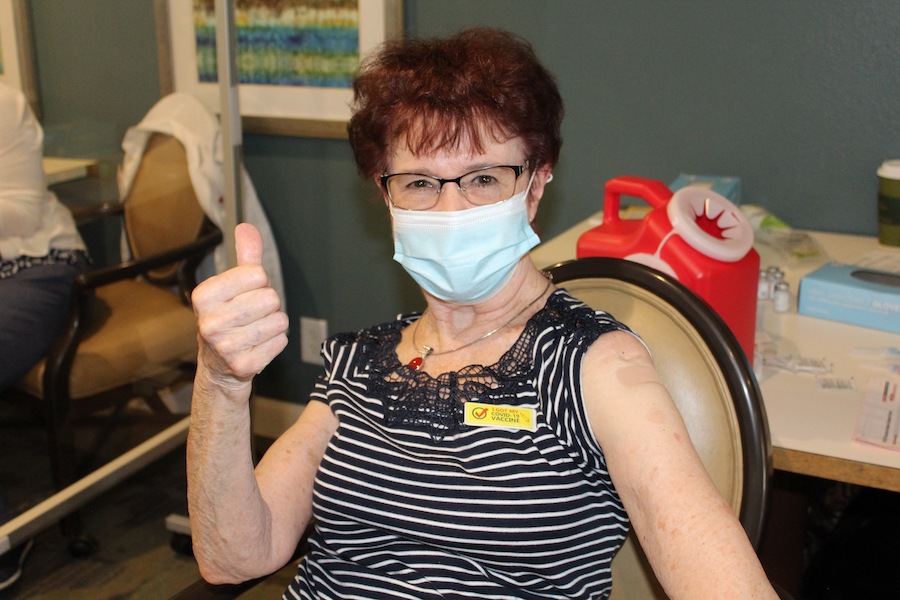A senior woman wearing a mask gives a thumbs up