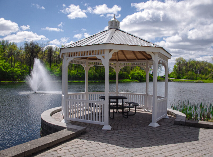 A white gazebo with a picnic table underneath, overlooking a large pond with a fountain