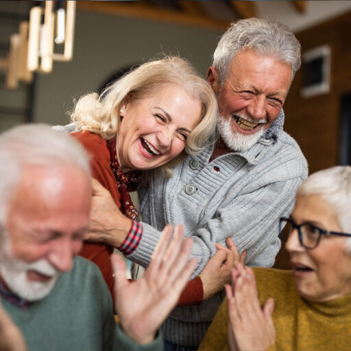 A group of four senior friends—two men and two women—laughing together.