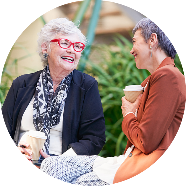 Two senior women chat and laugh outside over coffee