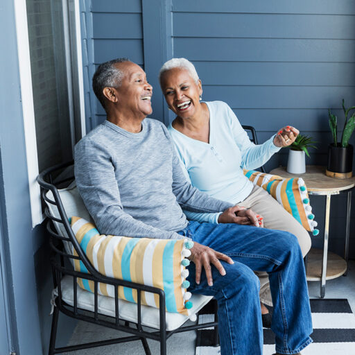 Senior man and woman chat and laugh on a porch chair