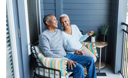 Senior man and woman chat and laugh on a porch chair