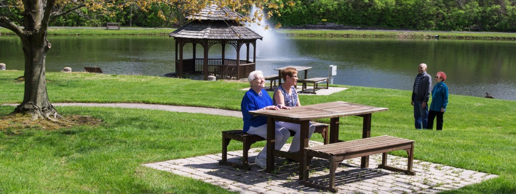 Seniors enjoying a sunny day in the garden near a lake at an independent living community