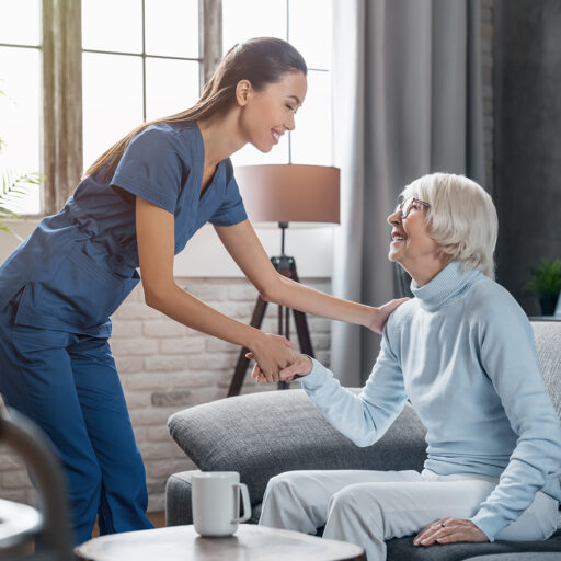 Registered nurse shakes hands with senior woman seated on a couch in a senior living facility