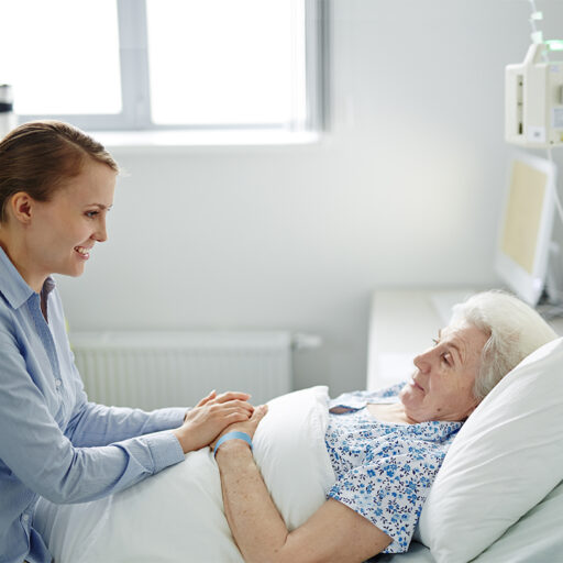 A senior woman laying in a bed receives hospice care while visiting with her daughter