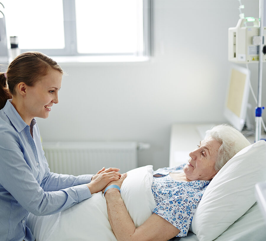 A senior woman laying in a bed receives hospice care while visiting with her daughter