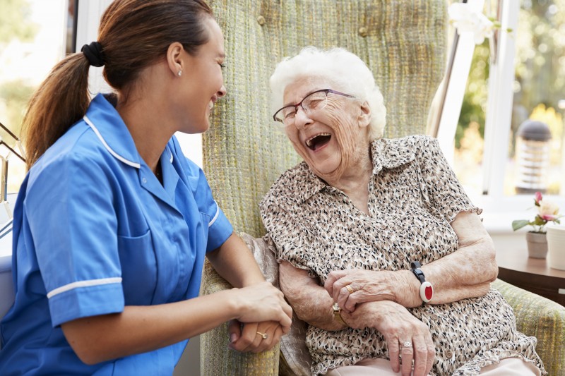 A senior woman and her professional caregiver chat at a memory care community.