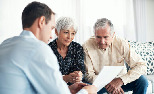 A young man discusses financial assistance for caregivers with a senior man and woman