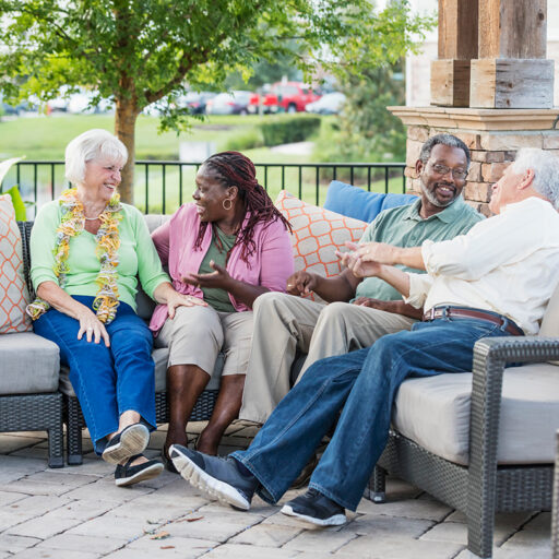 Two senior men and two senior women socialize outdoors on nice patio furniture
