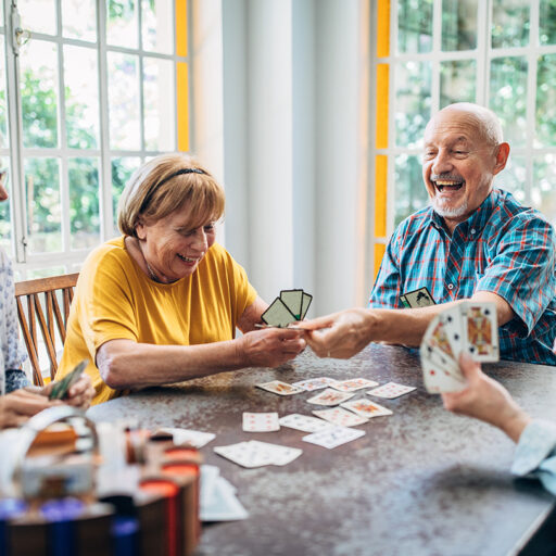 Three senior women and a senior man laugh over a game of poker.