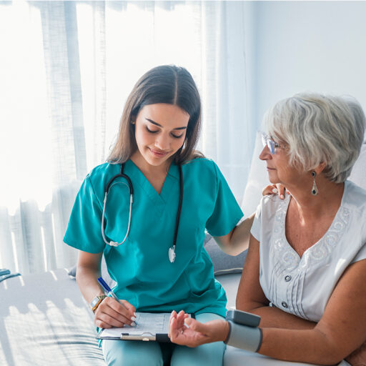 young skilled nursing professional checks the pulse of a senior woman and records the results on a clipboard