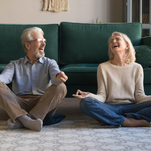 A senior man and a senior woman doing yoga on their living room floor