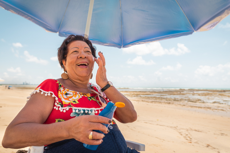 Senior woman applying sunscreen under an umbrella at the beach