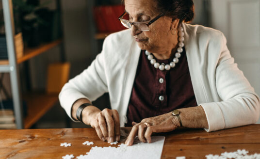 Senior woman putting together a puzzle on a wooden table, which is a great activity for seniors with dementia