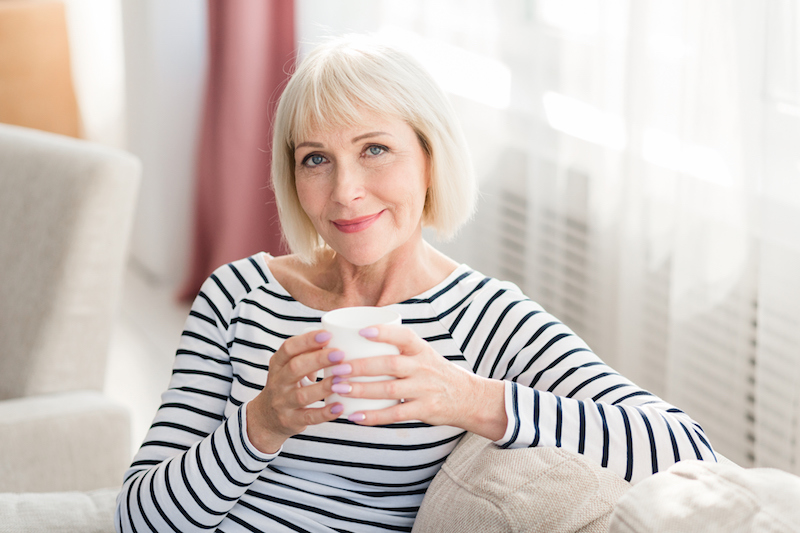 Senior woman drinks warm beverages on her living room couch to stay hydrated | Hydration Tips for Seniors