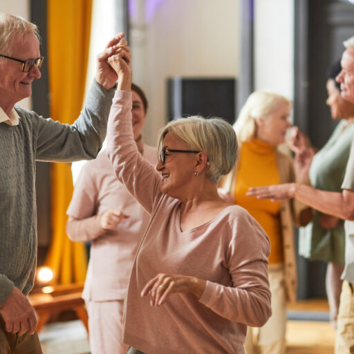 A group of smiling older people dancing together in an independent living community.