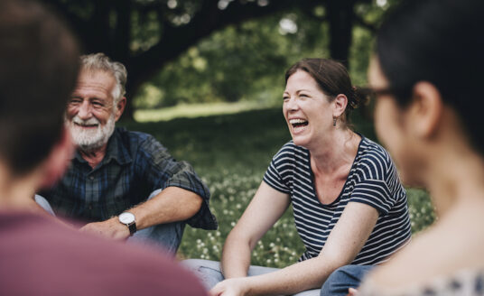 Older adults reap the benefits of nostalgia by reminiscing together, seated in a circle outdoors during springtime.