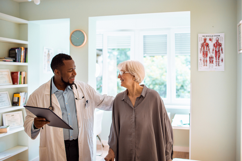 A senior woman receives preventive care for senior health issues by visiting and conversing with her male doctor in his office.