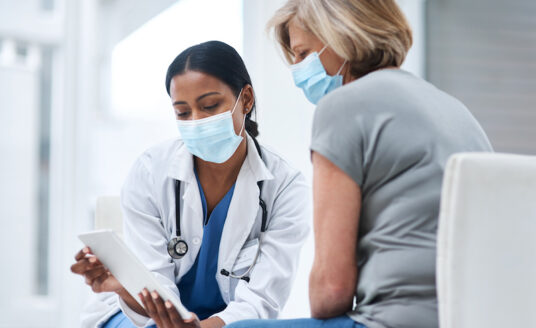 Senior woman receives health screenings from a female doctor, both of them are wearing masks