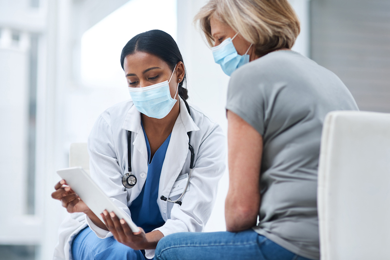 Senior woman receives health screenings from a female doctor, both of them are wearing masks