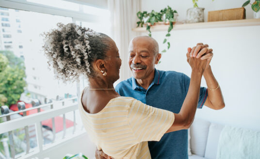 A senior man and woman enjoy the health benefits of dancing by dancing together in their home