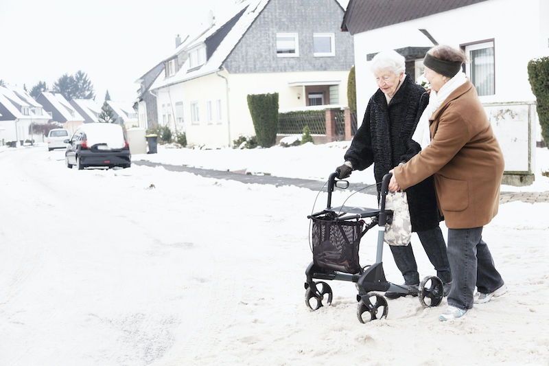 A senior woman with a walker practices fall prevention by traveling through the snow with a companion.