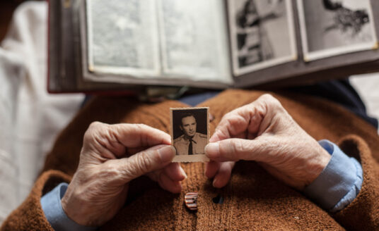 Senior holding old photo of young man, feeling the positive effects of memories and nostalgia