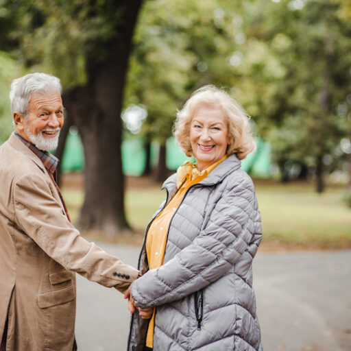 A senior man and woman hold hands in a park during the day time, before sundown syndrome affects the senior with dementia.