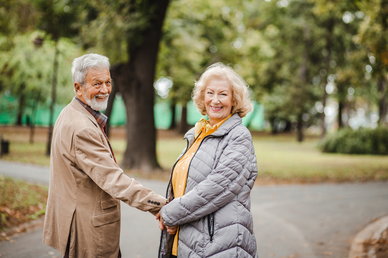 A senior man and woman hold hands in a park during the day time, before sundown syndrome affects the senior with dementia.
