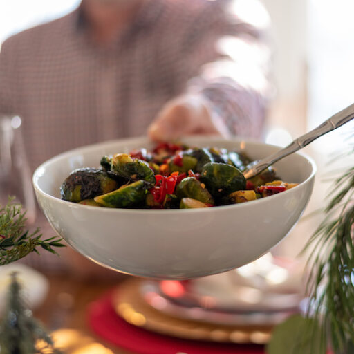A woman passes a bowl of green beans across the holiday dinner table, practicing healthy holiday eating tips