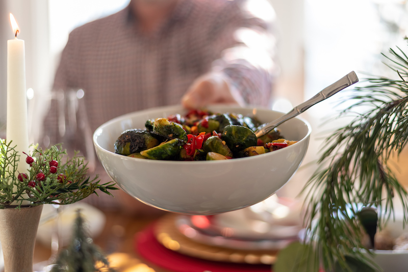 A woman passes a bowl of green beans across the holiday dinner table, practicing healthy holiday eating tips
