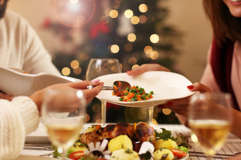 A group of people are seated around a holiday dinner table, passing a plate of food. The person serving food is managing diabetes by exercising portion control.
