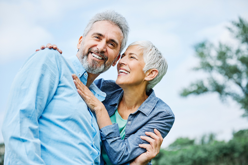 A senior man and woman embrace each other and smile outside as they stay motivated toward their health goals.