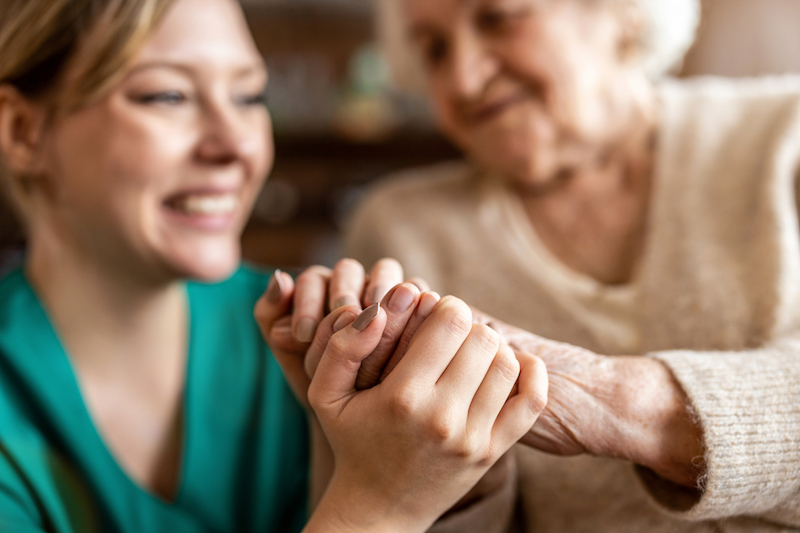A young woman and older woman hold hands and smile in a hospice care facility, despite hospice care myths they may have heard.