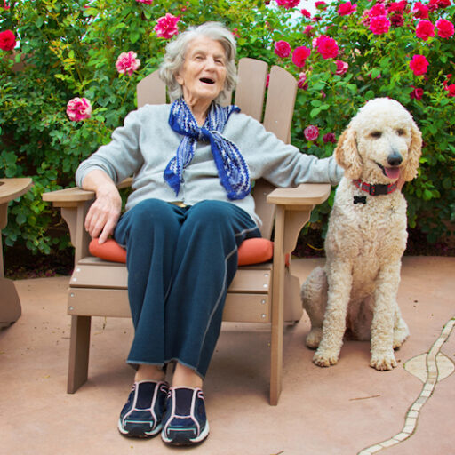 A senior woman with dementia seated outside and petting a dog, which acts as a sensory object
