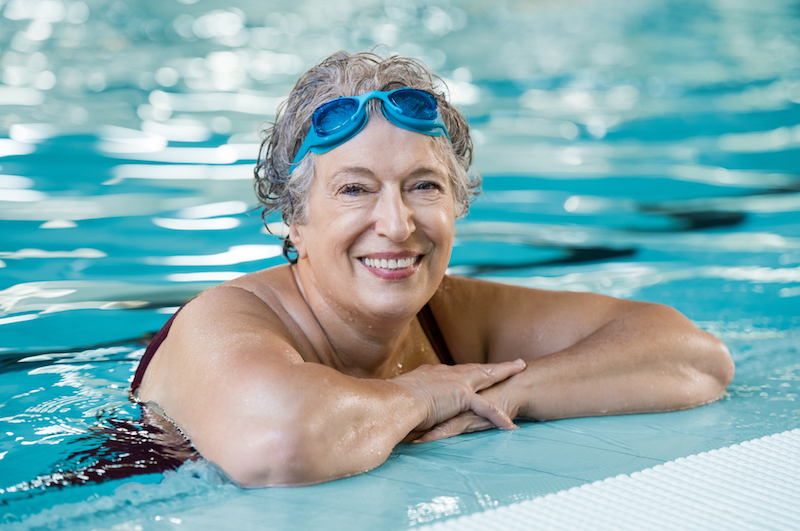 A senior woman smiles in a swimming pool as a way to get back into old hobbies.