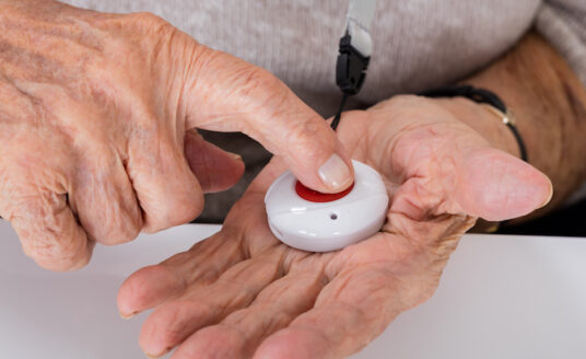 The hands of a senior man press the button on a medical alert system.