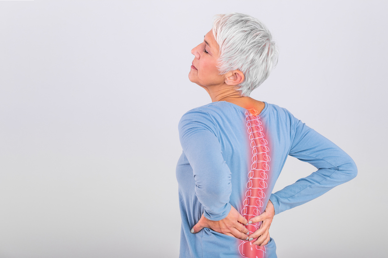 A senior woman in a blue shirt holds her back in pain, with a visual representation of her spine showing changes to posture.