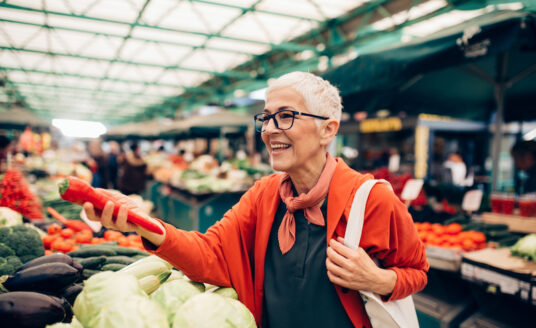 A senior woman holding produce in a farmers market as she practices healthy nutrition for seniors.