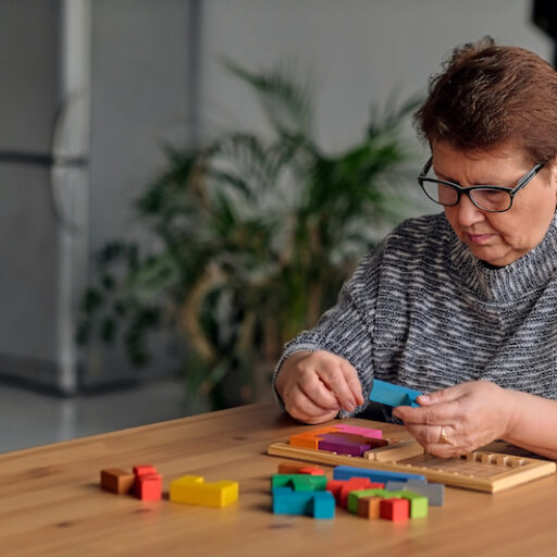 An older woman puts together a colorful wooden puzzle on a dining room table as one of many brain exercises.