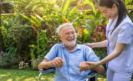 senior man living with dementia outside laughing with his care giver