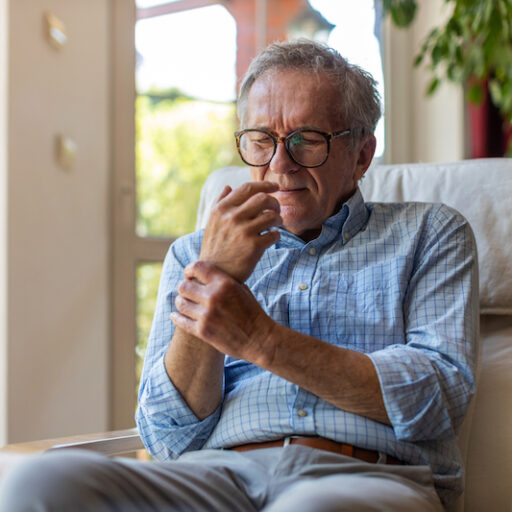 Senior man sitting down and struggling with chronic pain management.
