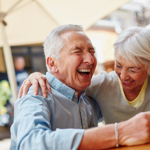 An older man and woman embrace each other and smile with laughter