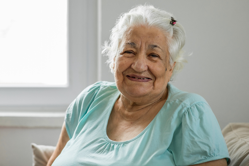 An older woman suffering from dementia smiles at the camera.