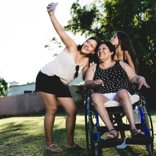 older women in a wheelchair taking a picture with two younger women in the park while doing activities for seniors