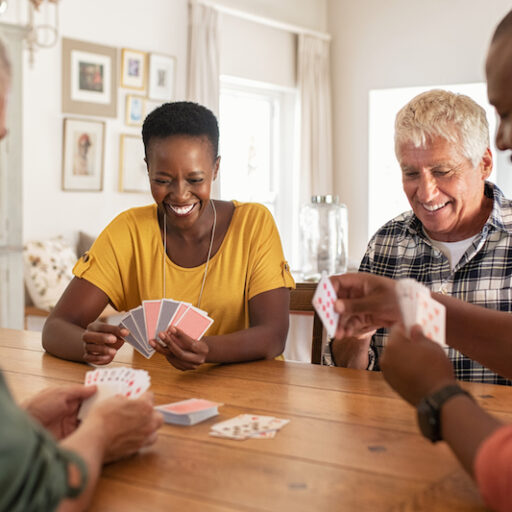 A group of seniors gather around a table to play cards indoors, an example of safe summer activities for seniors.